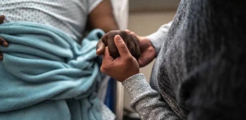 individual holding a loved one's hand in a hospital bed